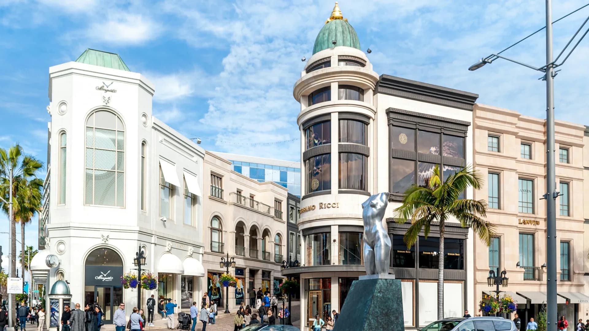 Rodeo Drive in Beverly Hills, storefronts along the street and a domed corner building with palms on the sidewalk
