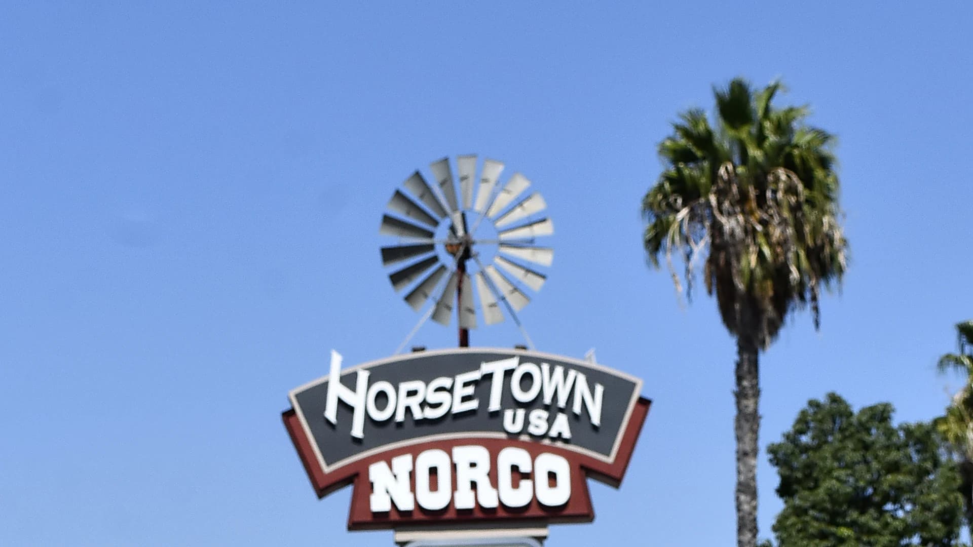 The Horsetown USA sign at the edge of Norco, a steel farm windmill mounted above a shield reading HorseTown USA over Norco, with a fan palm beside it against a clear sky