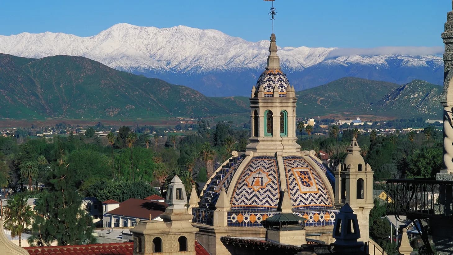 The tiled dome of the St. Francis Chapel at the Mission Inn in downtown Riverside, with the snow-covered San Bernardino Mountains rising behind the city.