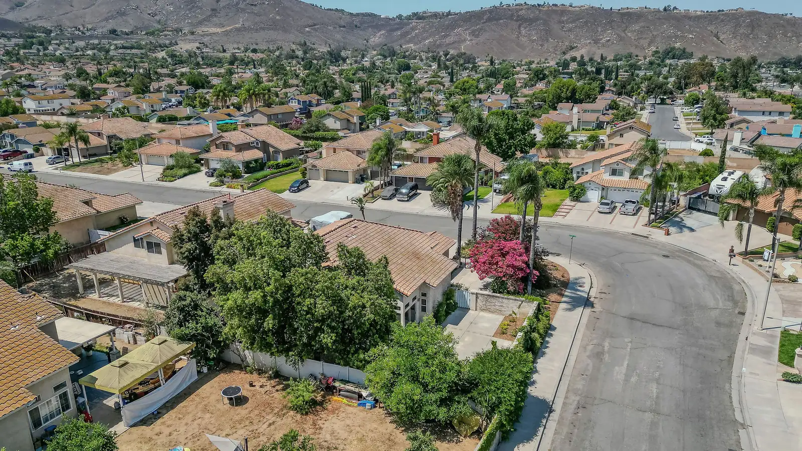 Aerial view of a Riverside, California neighborhood of tile-roofed single-family homes around a cul-de-sac, with dry hills rising behind.