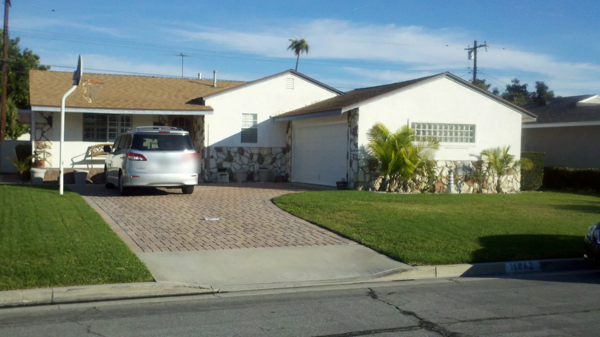 Single-story California home with a wide paver driveway, attached garage and palm planting along the front