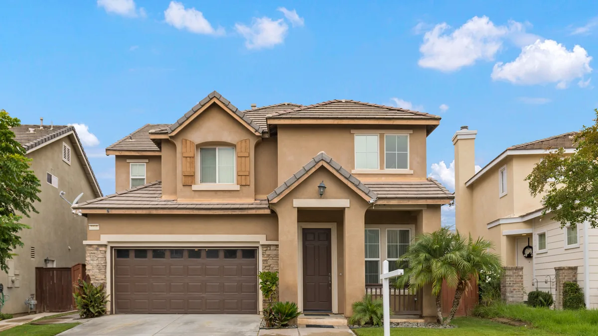 Newly built two-story home with a tile roof, stone-faced garage and fresh landscaping between two neighbors of the same vintage