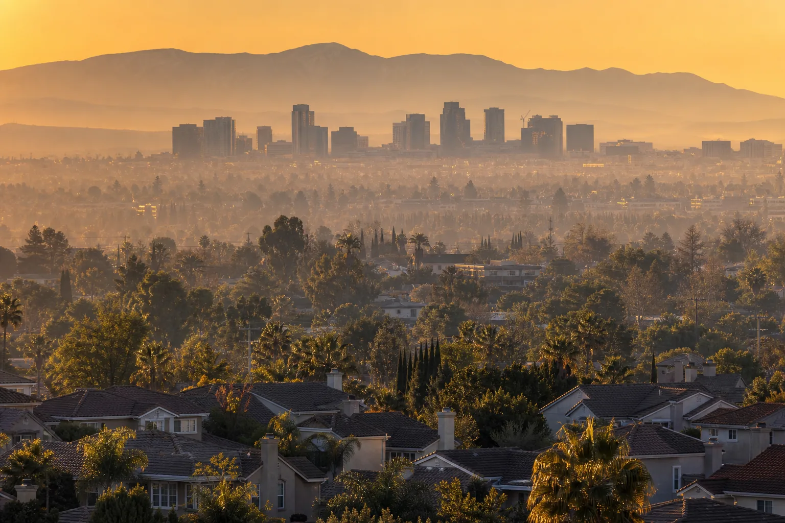 Aerial view at golden hour of an Inland Empire neighborhood of tile-roofed homes along curving streets, with dry hills in the distance