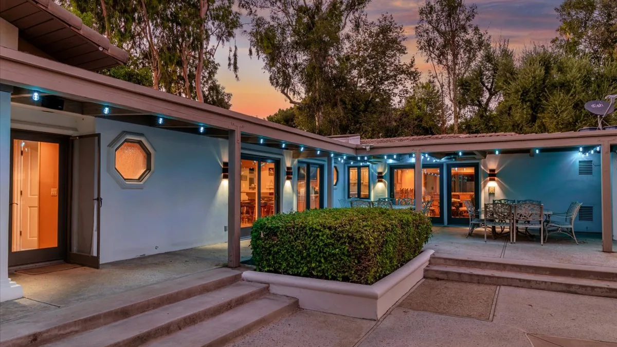 Courtyard of a mid-century modern home at twilight, pale blue walls, string lights overhead and warm light from the windows