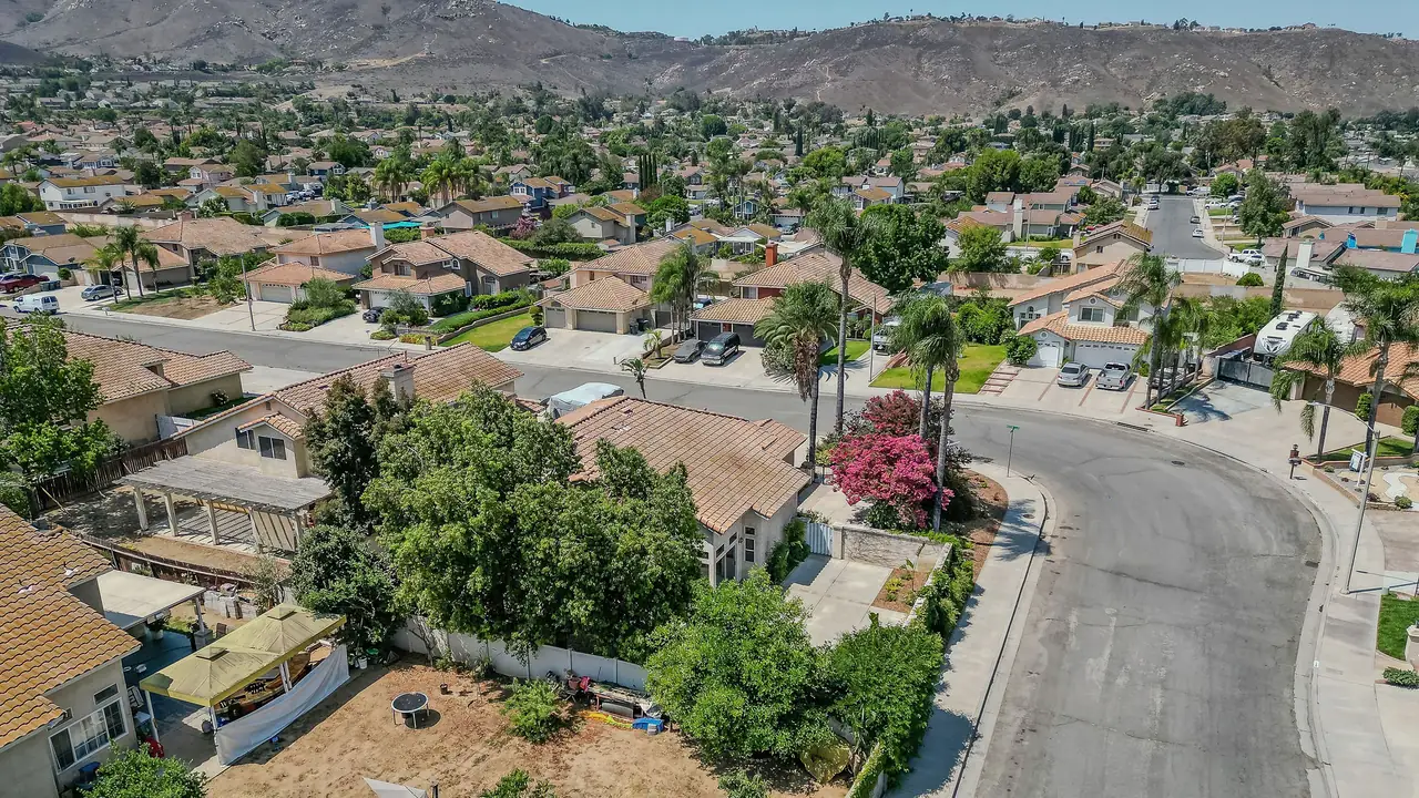 Aerial view of a Riverside neighborhood of tile-roofed single-family homes along a curving street, with dry hills rising behind