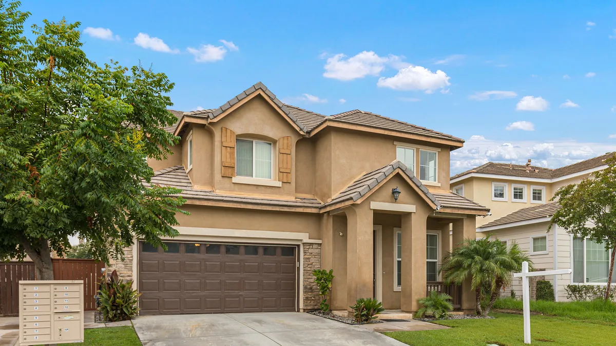 Two-story stucco home with a tile roof and attached garage in a newer Riverside County subdivision, a cluster mailbox at the curb